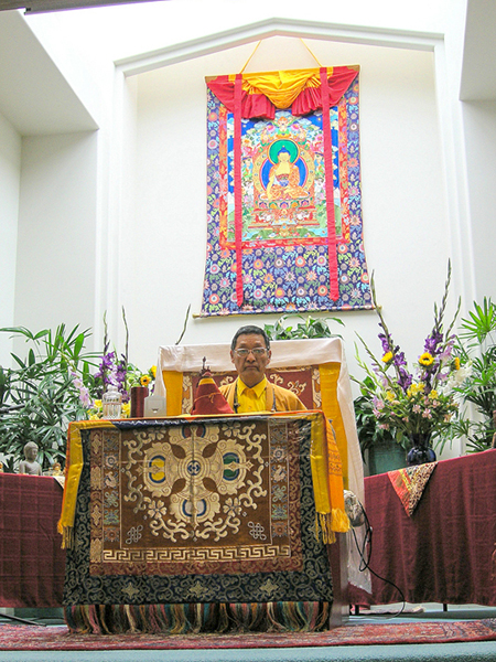 Gangteng Rinpoche teaching before a large appliqué thangka by Leslie Rinchen-Wongmo at Unity Church in Santa Barbara, CA in 2014
